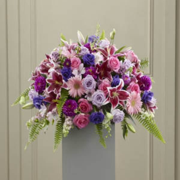 Mixed pink, purple, and white flowers arranged in a tall pedestal vase