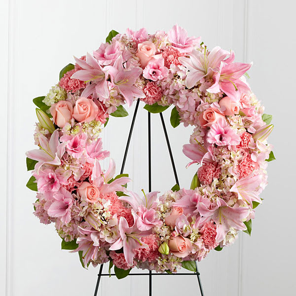 Pink floral wreath with lilies, roses, and carnations on a black stand