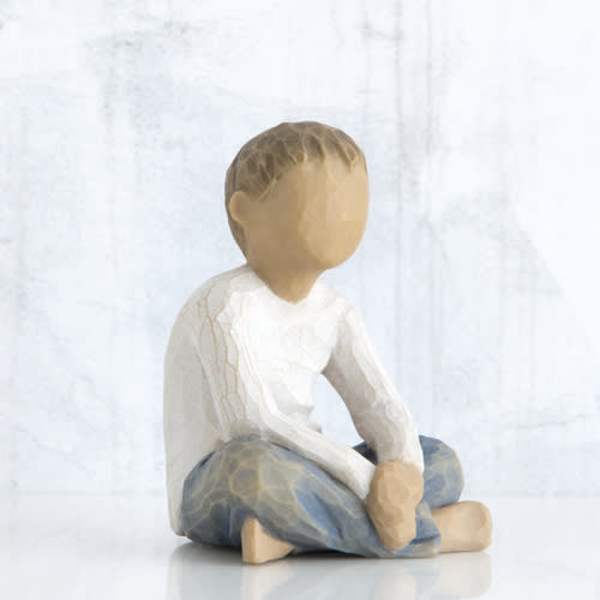 Wooden figurine of a seated child in a white shirt and blue pants