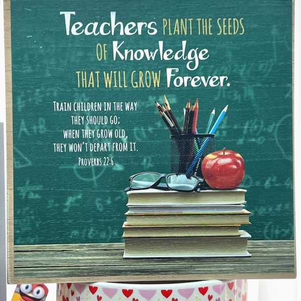 Teacher-themed sign with books, pencils, glasses, and an apple