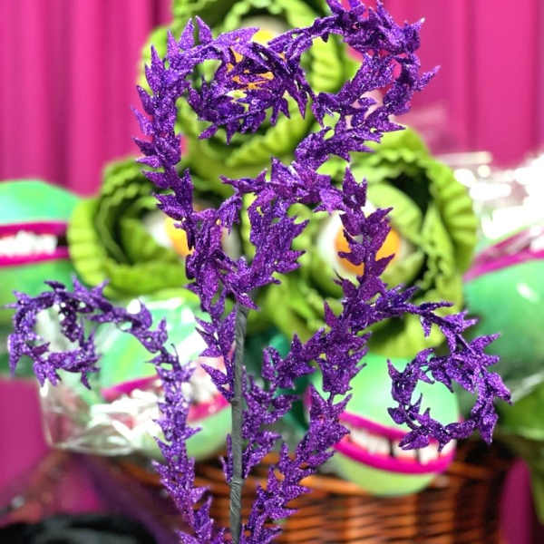 Purple glittery decorative stem in front of green gift baskets