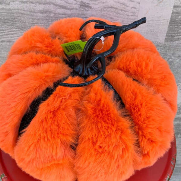Orange faux fur pumpkin decoration with a black stem on a red base