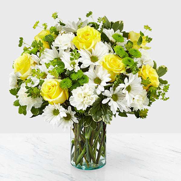 Arrangement of yellow roses, white daisies, and green button poms in a clear glass vase