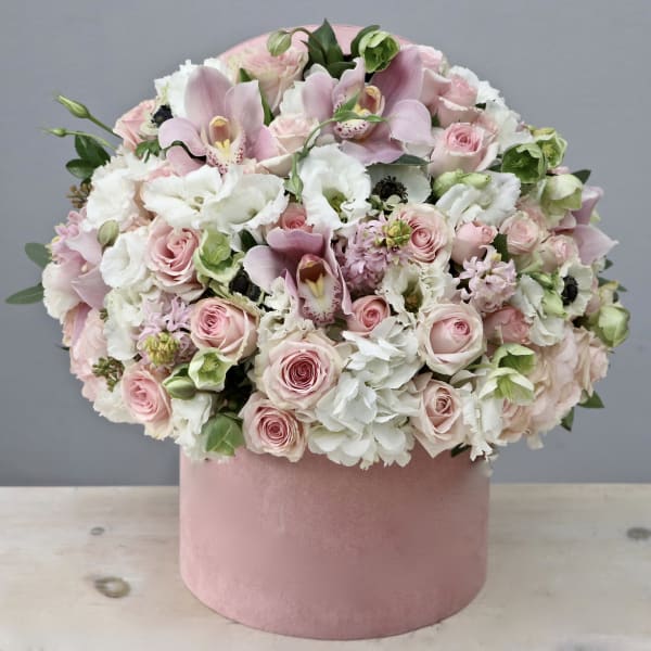 Low pink and white flower arrangement with orchids and roses in a round pink hat box