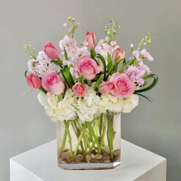 Pink roses and tulips with white hydrangeas in a clear square glass vase with stones