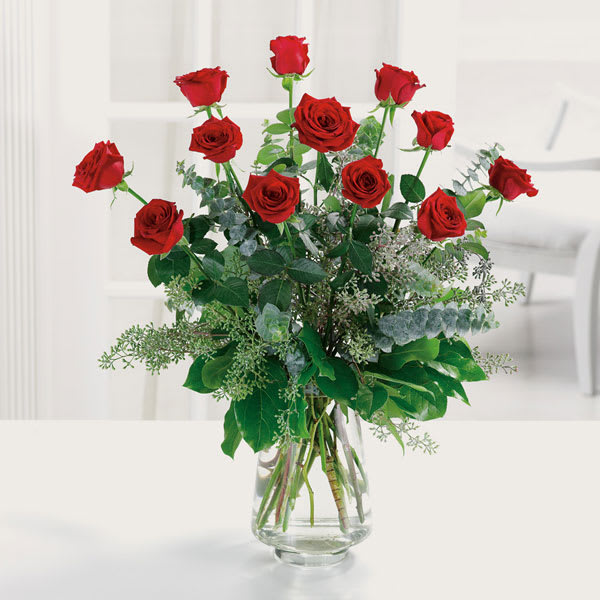 Red roses arranged in a clear glass vase with greenery