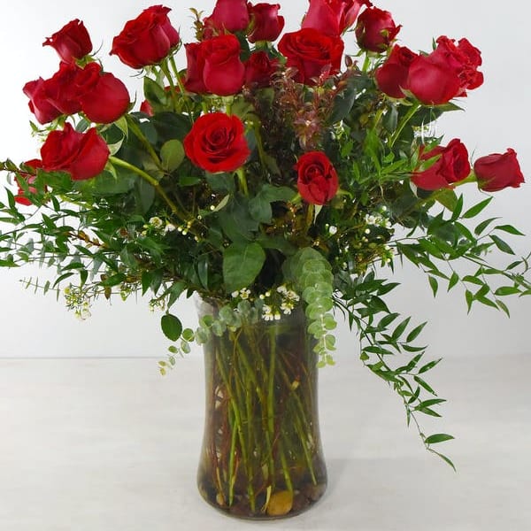 Red roses arranged in a clear glass vase with greenery
