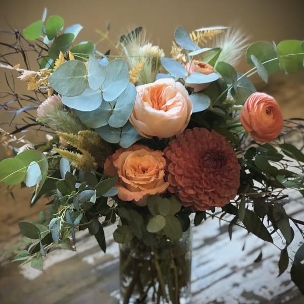 Peach and coral bouquet in a glass vase with blue-green foliage
