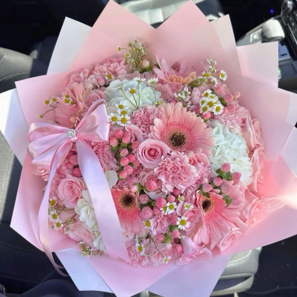 Pink and white hand-tied bouquet with gerbera daisies, roses, and small daisies wrapped in pink paper with a bow