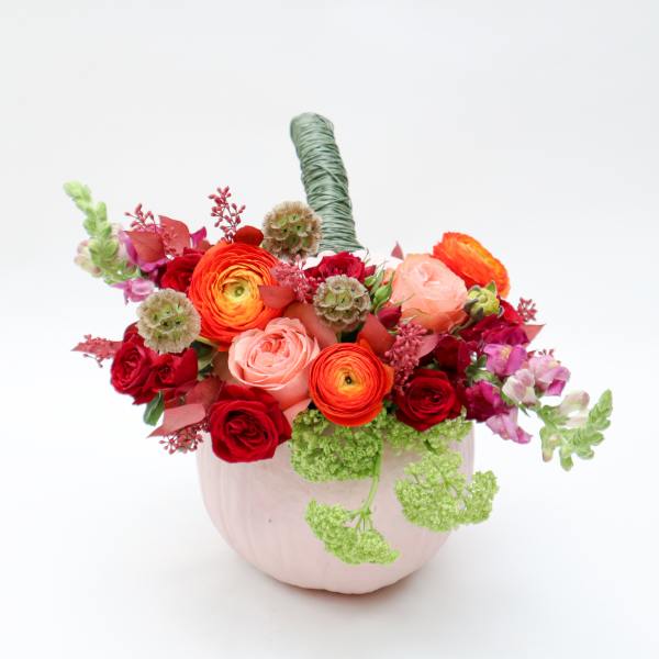 Mixed bouquet of red, pink, and orange flowers in a pale pink vase