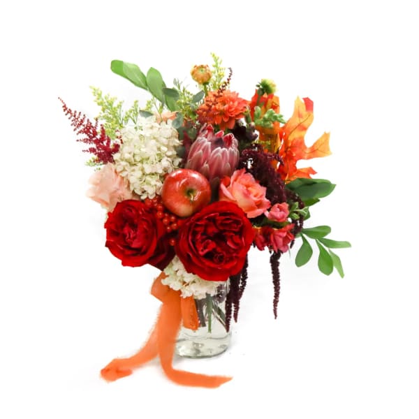 Mixed bouquet of red roses, white hydrangea, and autumn accents in a glass vase