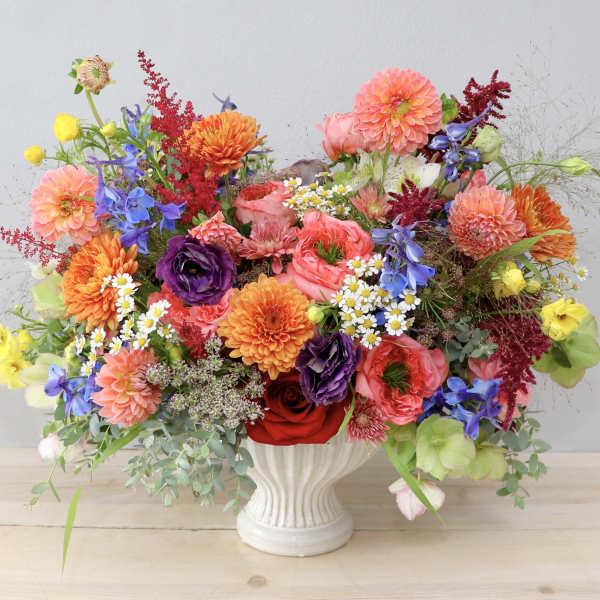 Colorful mixed bouquet in a white vase with dahlias, roses, and blue flowers