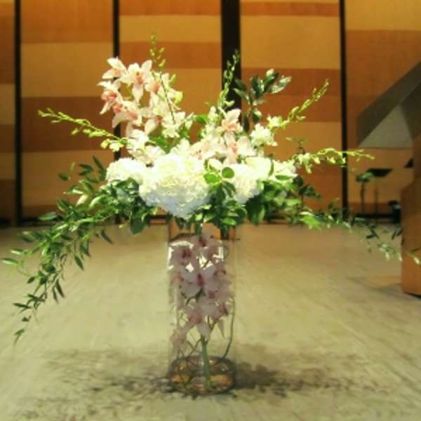Tall arrangement of white hydrangeas and pink orchids with trailing greenery in a clear glass vase