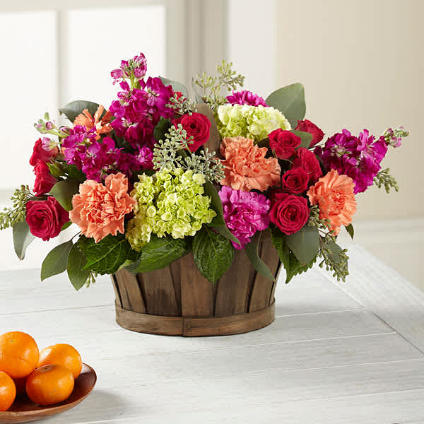 Mixed bouquet in a wooden basket with pink, coral, and green blooms