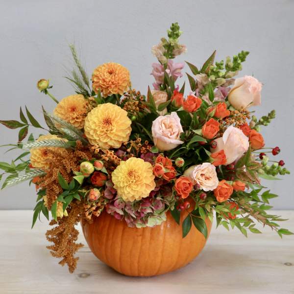 Autumn arrangement of orange and peach flowers in a hollow pumpkin container
