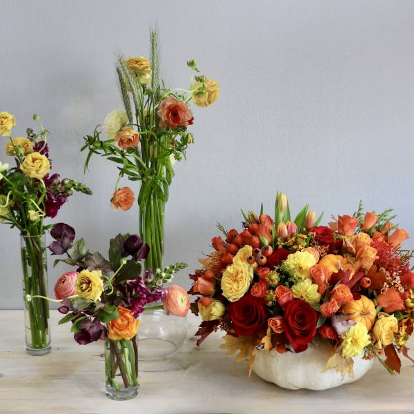 Autumn centerpiece of orange and yellow flowers in a white pumpkin with three smaller mixed bud vases.