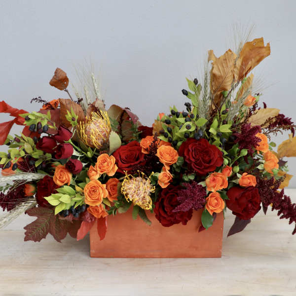 Low rectangular arrangement of red and orange roses with pincushion protea in an orange container