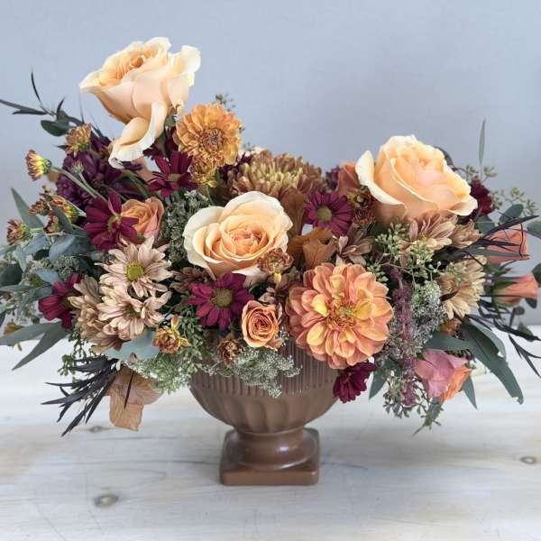 Low centerpiece of peach roses and mixed autumn flowers in a brown pedestal bowl