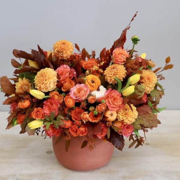 Low orange and yellow autumn flower arrangement with roses and dahlias in a terracotta pot.