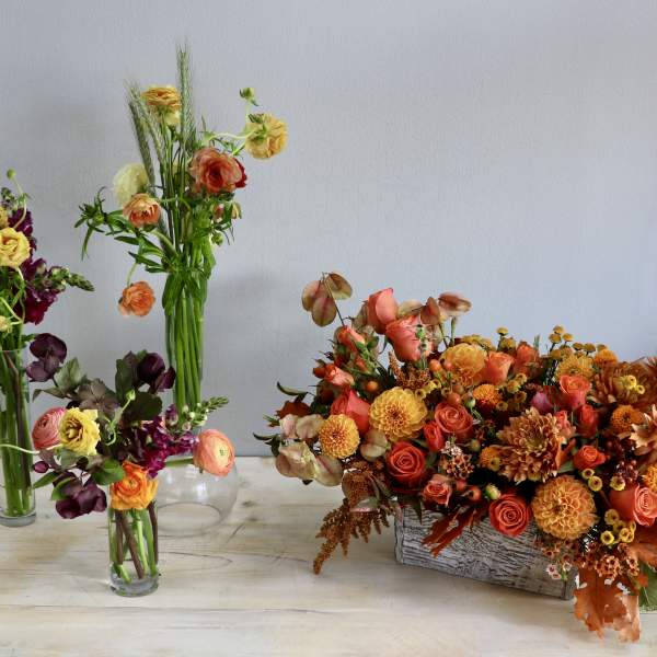Set of orange and yellow mixed flower arrangements in glass vases and a rustic rectangular container