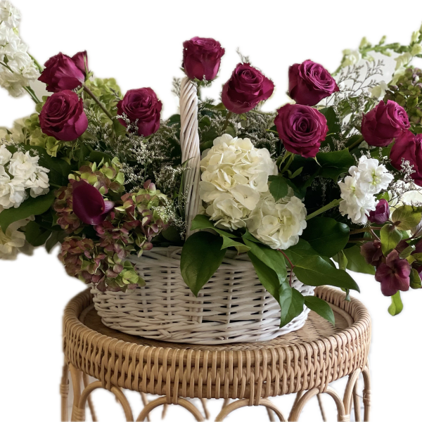 Basket arrangement of magenta roses, white hydrangeas, and white stock