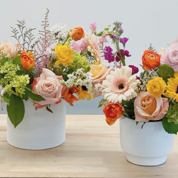 Two colorful flower arrangements in white pots on a table