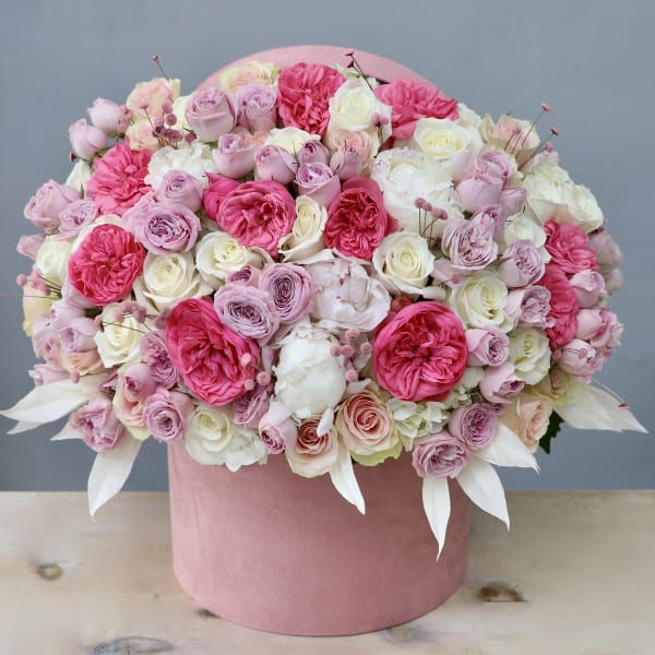Dense arrangement of pink and white roses and peonies in a round pink hatbox container