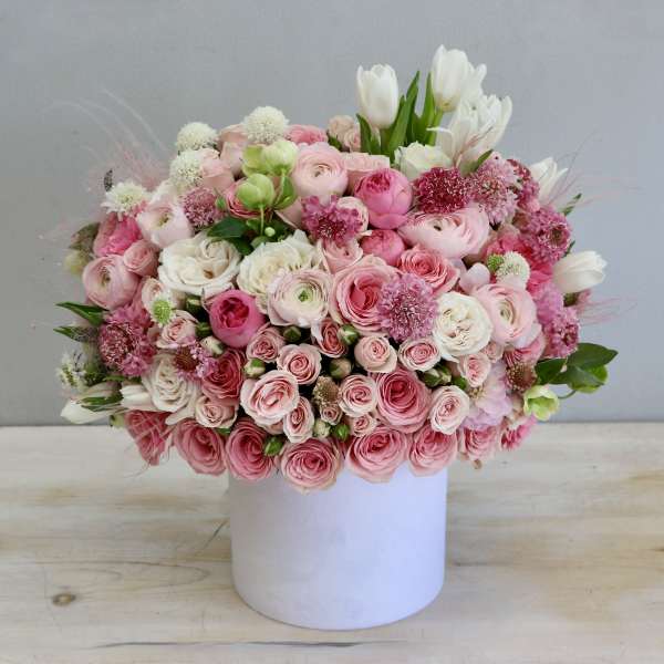 Round arrangement of pink and white roses and ranunculus in a white cylinder container