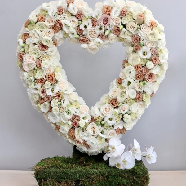 Heart-shaped standing wreath of ivory and blush roses on a moss-covered base with white orchids at the bottom