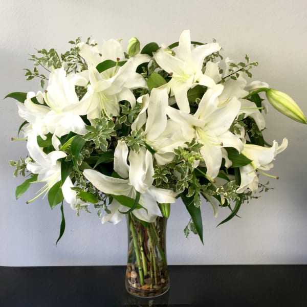 Tall clear vase of white lilies with variegated foliage