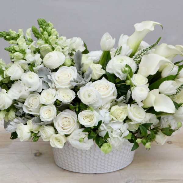 Low white arrangement of roses, calla lilies, tulips, and snapdragons in a round ceramic bowl