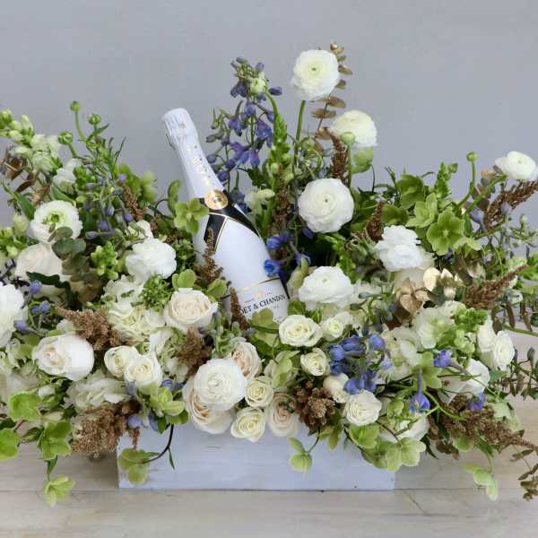 Low white box arrangement of white and green flowers with a champagne bottle nestled in the center