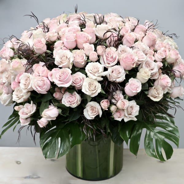 Large dome arrangement of pale pink and white roses in a green glass cylinder vase