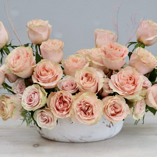 Low arrangement of pale peach roses in an oval white bowl
