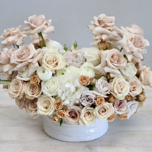 Low arrangement of cream and blush roses with white blooms in a round white ceramic bowl
