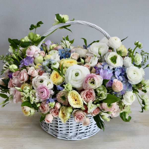 Pastel basket arrangement of white ranunculus, pink roses, and yellow blooms in a white wicker basket