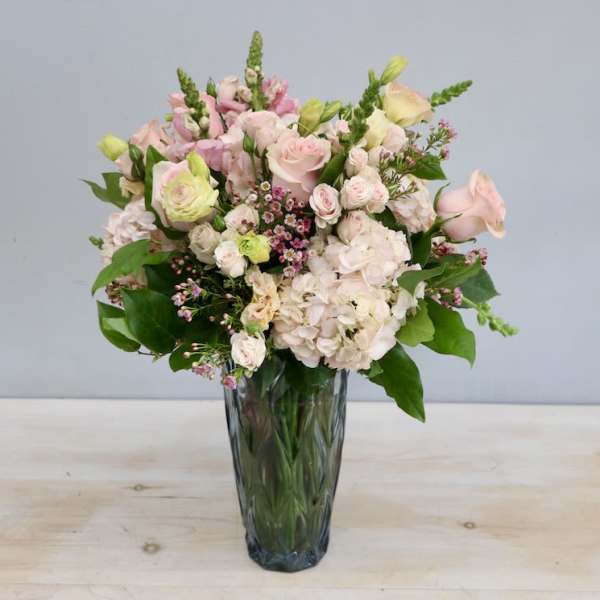 Tall arrangement of pale pink roses and hydrangeas with accent blooms in a faceted glass vase