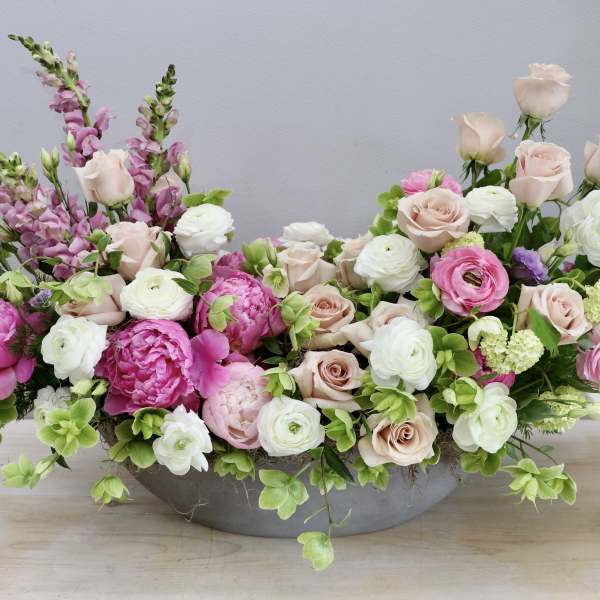Low oval centerpiece of pink peonies, blush roses and white ranunculus in a gray container