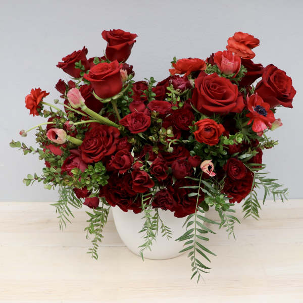 Lush arrangement of deep red roses and mixed red blooms in a white round vase