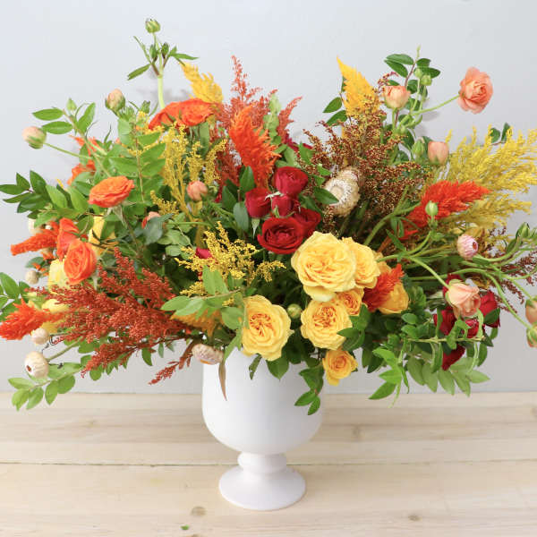 Colorful bouquet of roses and mixed blooms in a white pedestal vase