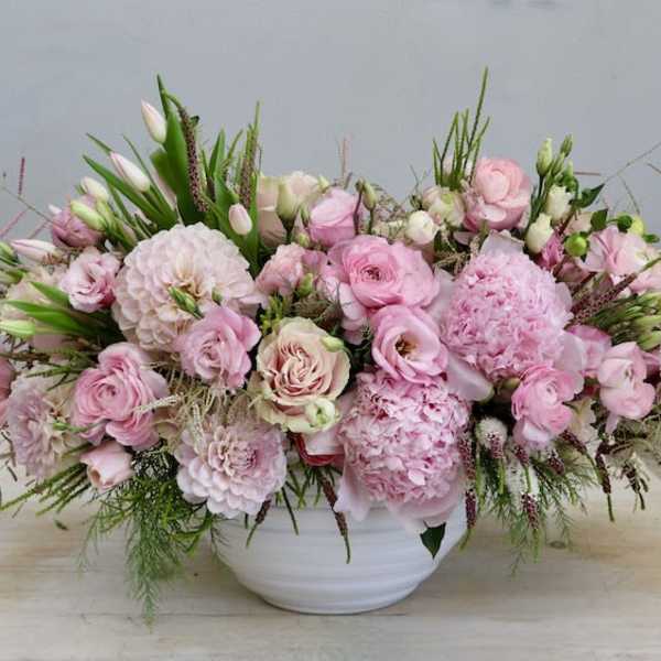 Low pink arrangement of roses, peonies, and other blooms in a white ceramic bowl
