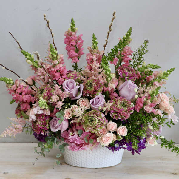 Lush pink and lavender flower arrangement with roses and snapdragons in a white ceramic bowl