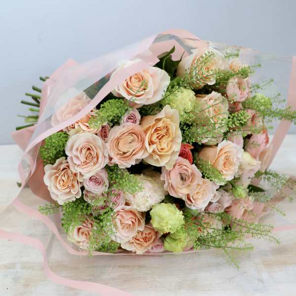 Bouquet of peach roses with lime-green accents wrapped in pink and clear cellophane