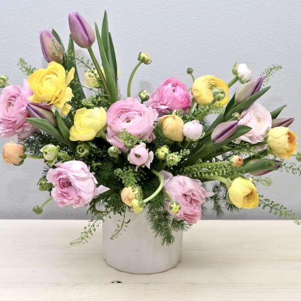 Pastel pink, yellow, and purple ranunculus and tulips in a white ceramic vase