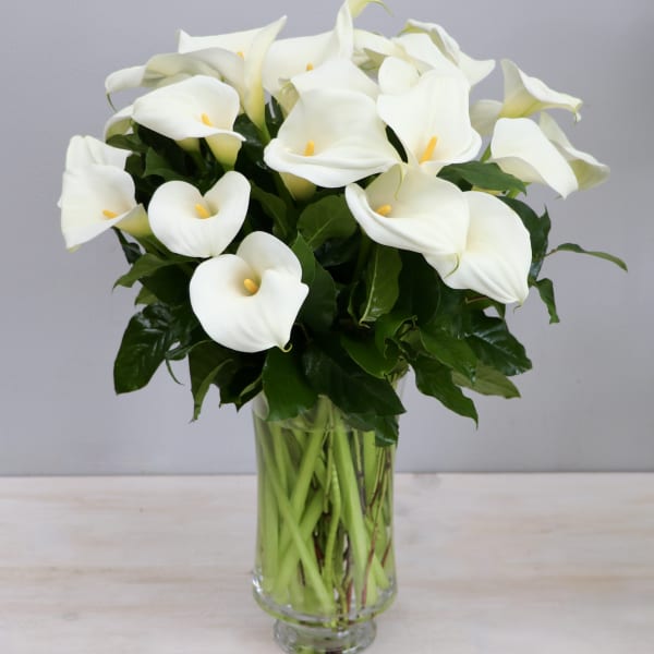 Tall arrangement of white calla lilies in a clear glass vase