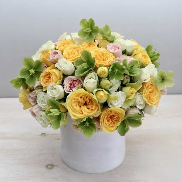Low arrangement of yellow and pastel roses with green blooms in a white ceramic cylinder vase