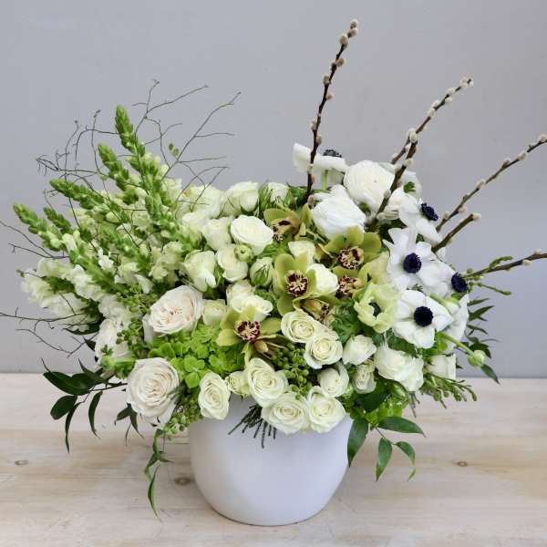 Asymmetrical white and green floral arrangement in a white ceramic pot