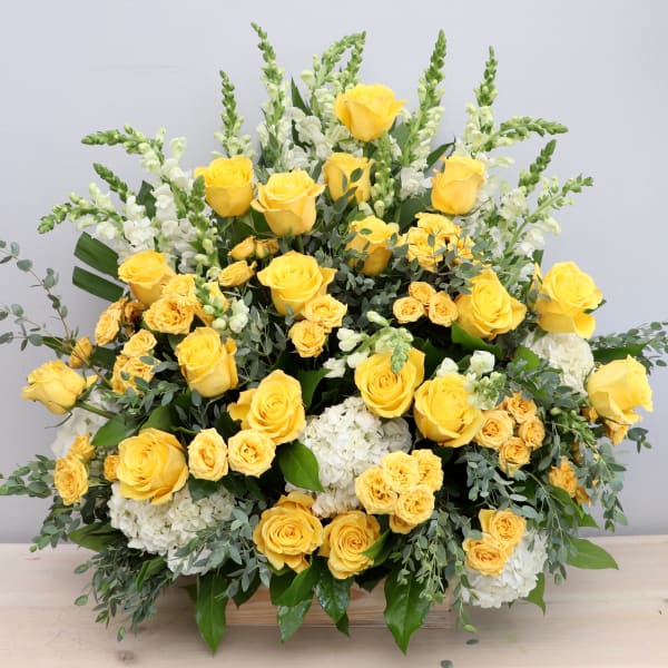 Large arrangement of yellow roses, yellow spray roses, white hydrangeas, and white snapdragons in a wooden container