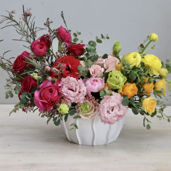 Low centerpiece of red, pink, yellow, and orange flowers in a white ceramic bowl.