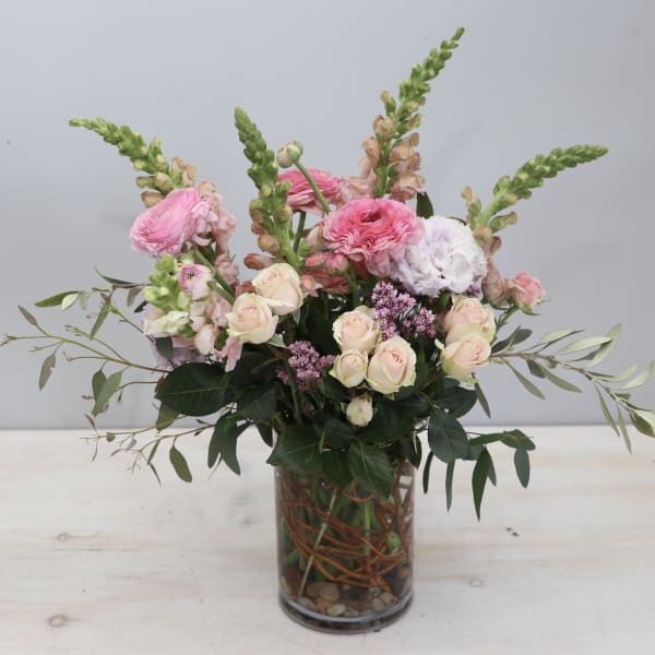 Tall pastel pink and white flower arrangement with roses and ranunculus in a clear glass vase.